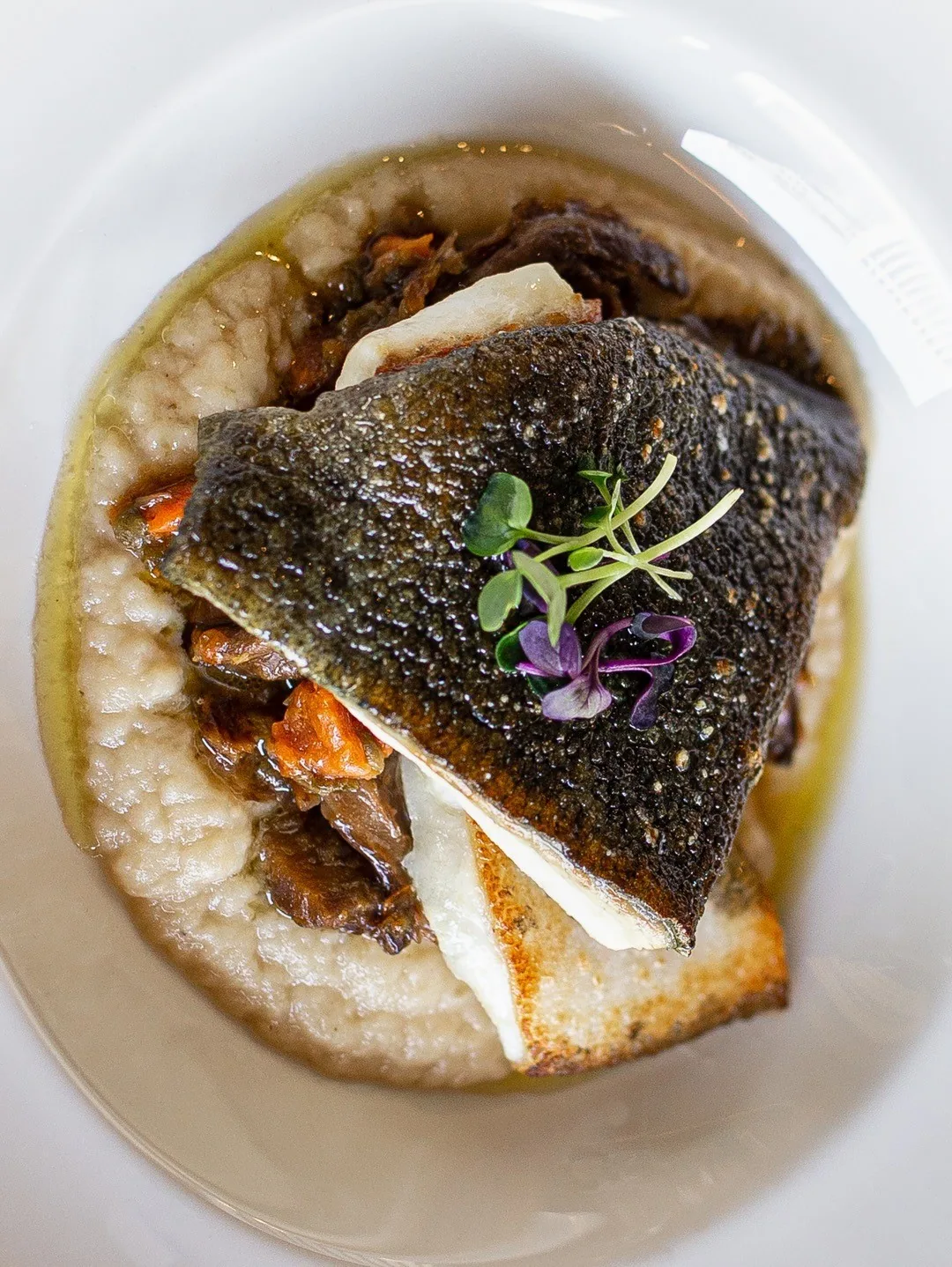 A crisp-skinned fish fillet on a bed of rice in a white bowl