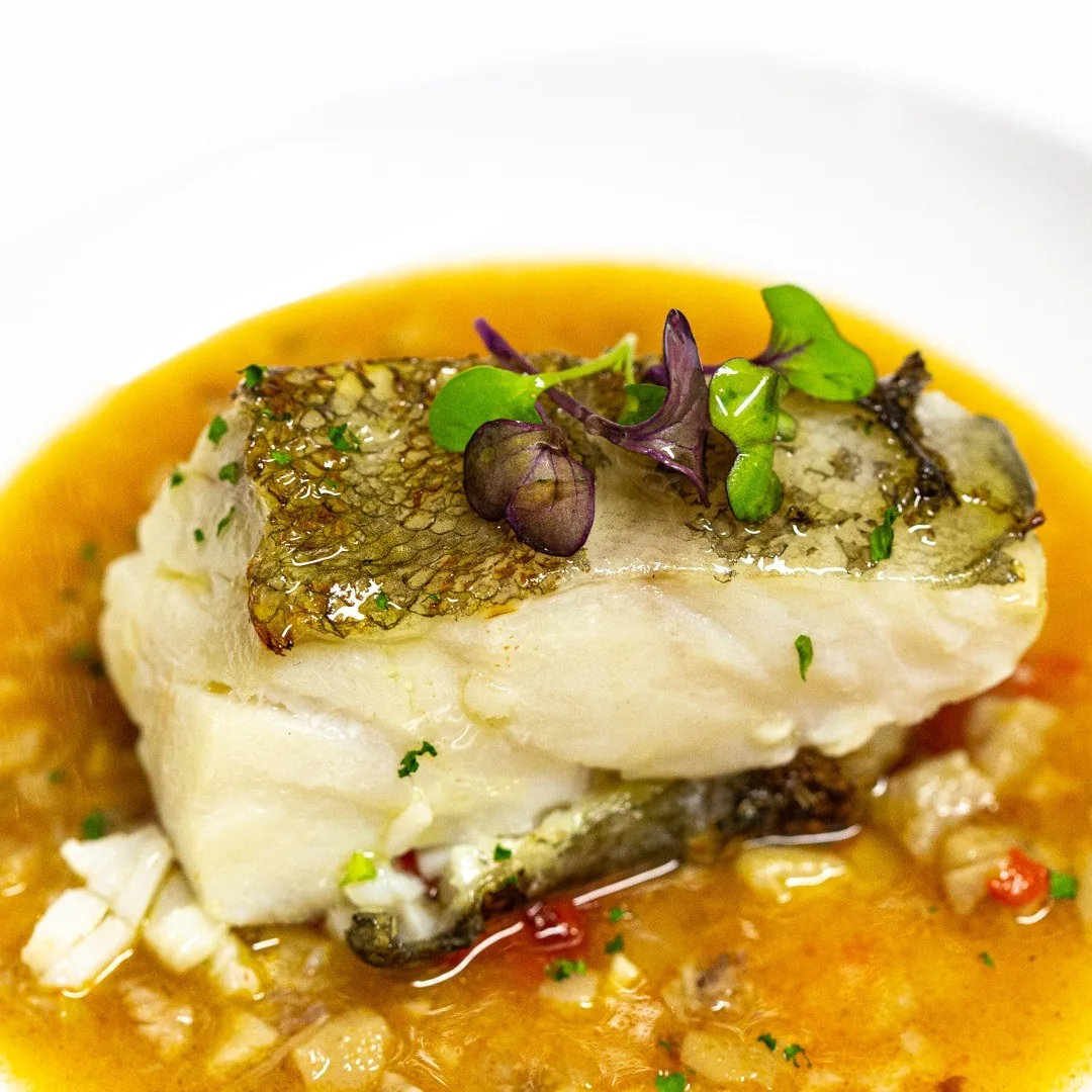 A fish fillet with skin on in a yellow sauce
