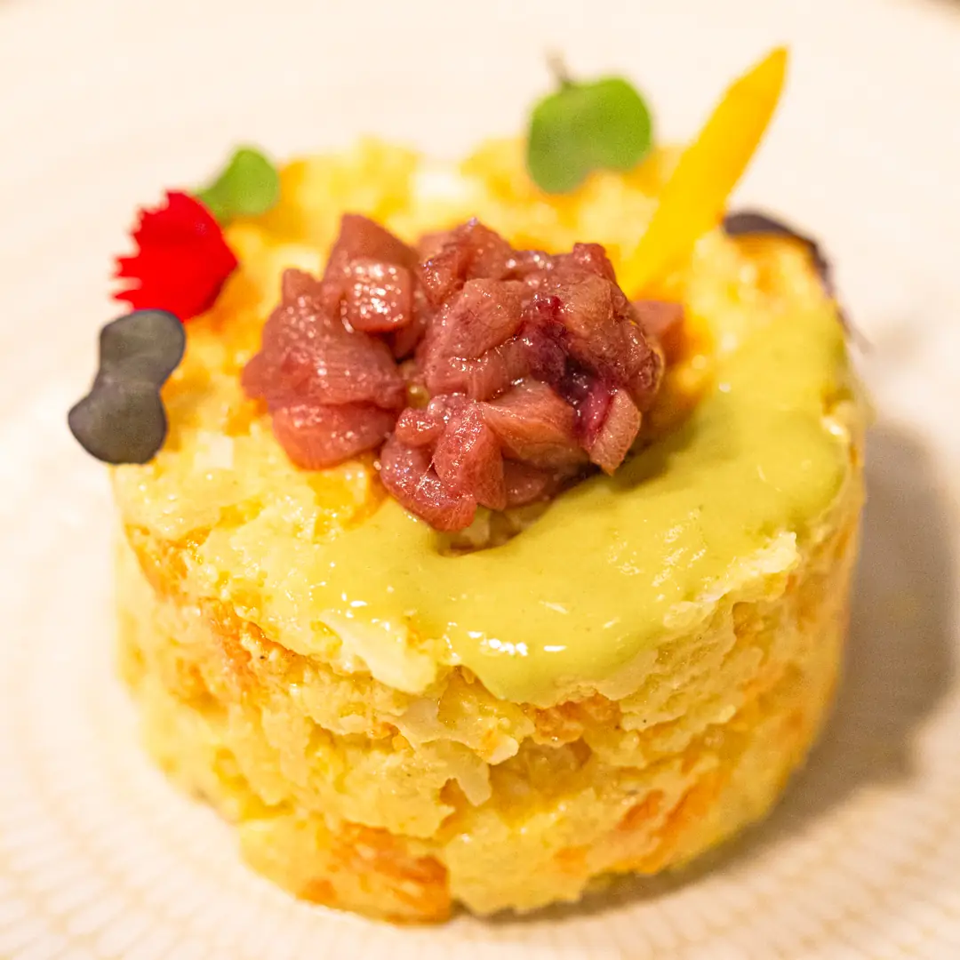 Rice cake topped with diced tuna tartare, avocado cream and edible flower garnish