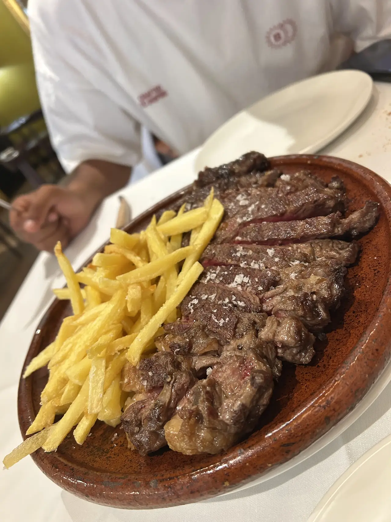 Sliced grilled steak with coarse salt served alongside french fries on a clay platter