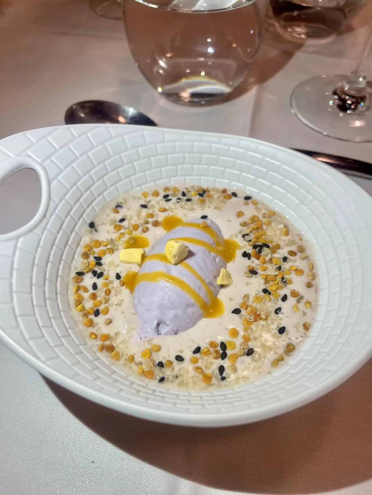 Purple sorbet quenelle with mango sauce and seed garnish in a pool of cream in a white bowl