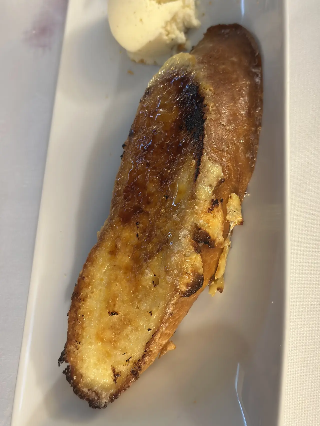 Caramelized torrija-style dessert with a scoop of ice cream on a rectangular plate