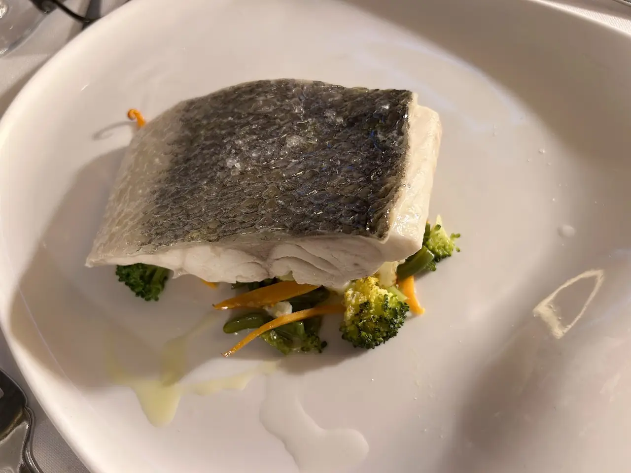Skin-on fish fillet plated over broccoli, green beans and carrot strips