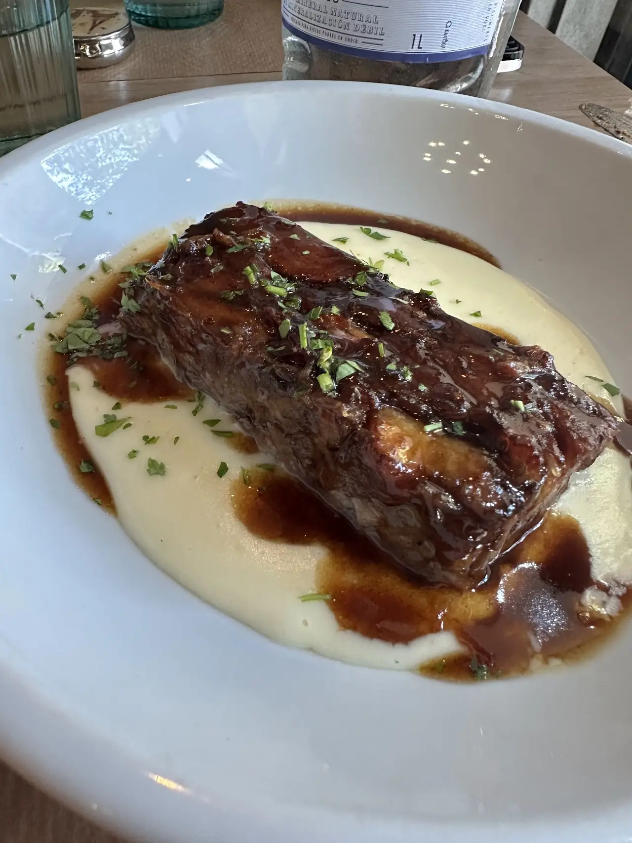 A braised short rib in sauce over a puree, on a white plate.