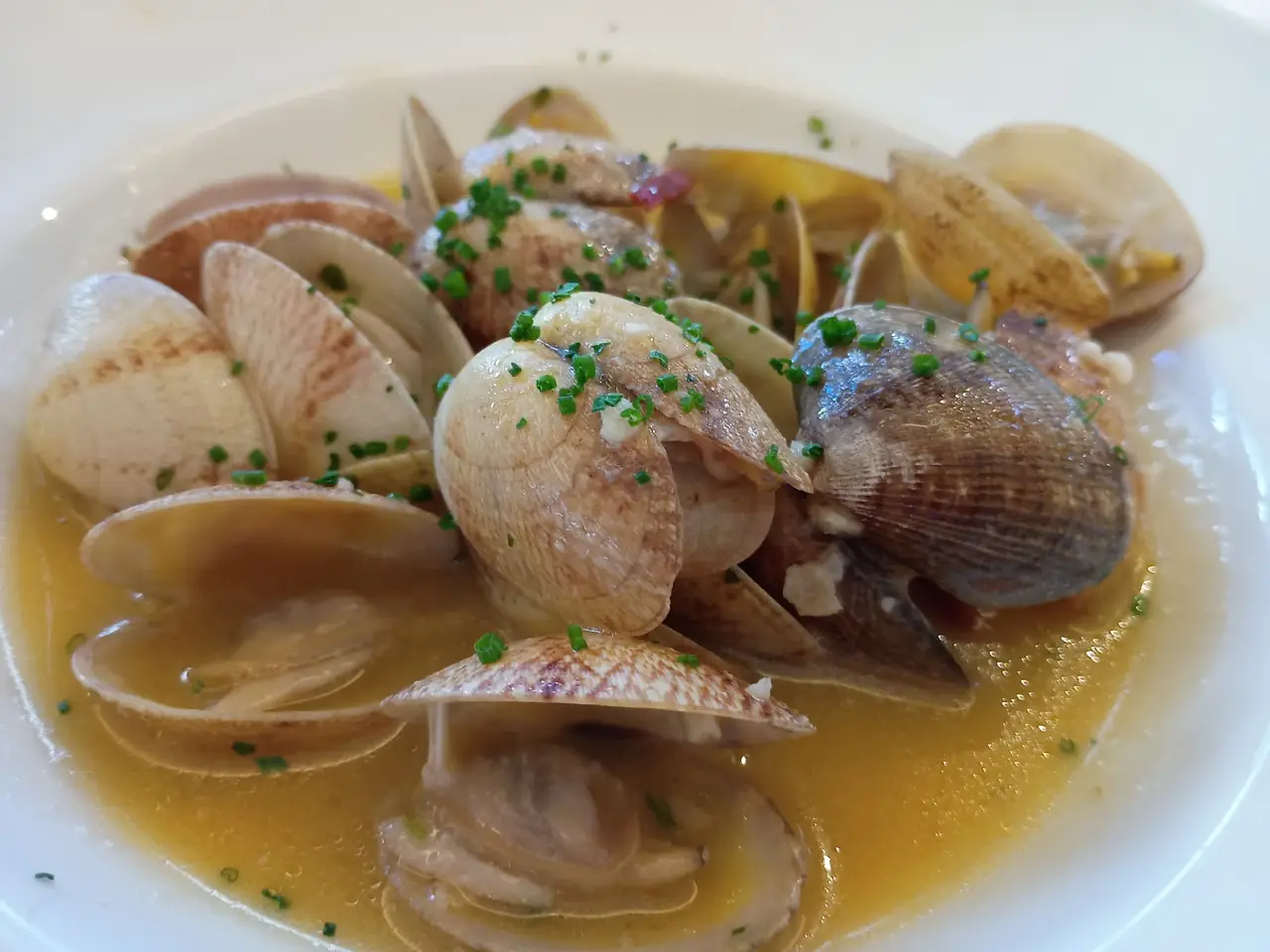 Bowl of clams in a garlic and white wine broth garnished with chopped chives