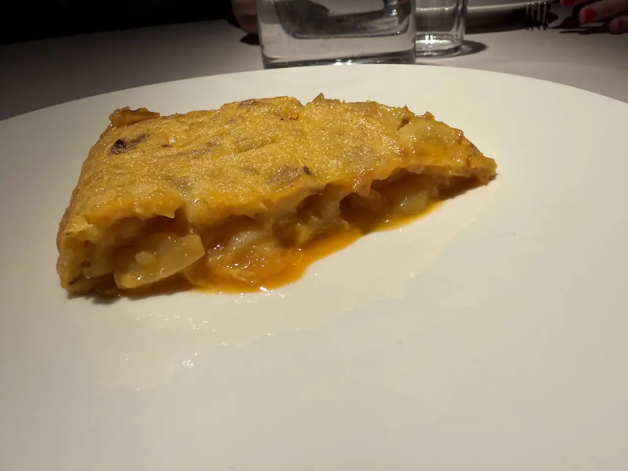 Wedge of Spanish tortilla with runny egg and potato on a plain white plate