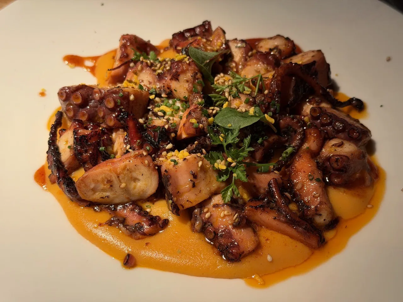 A plate of glazed pieces of octopus in an orange sauce with herbs