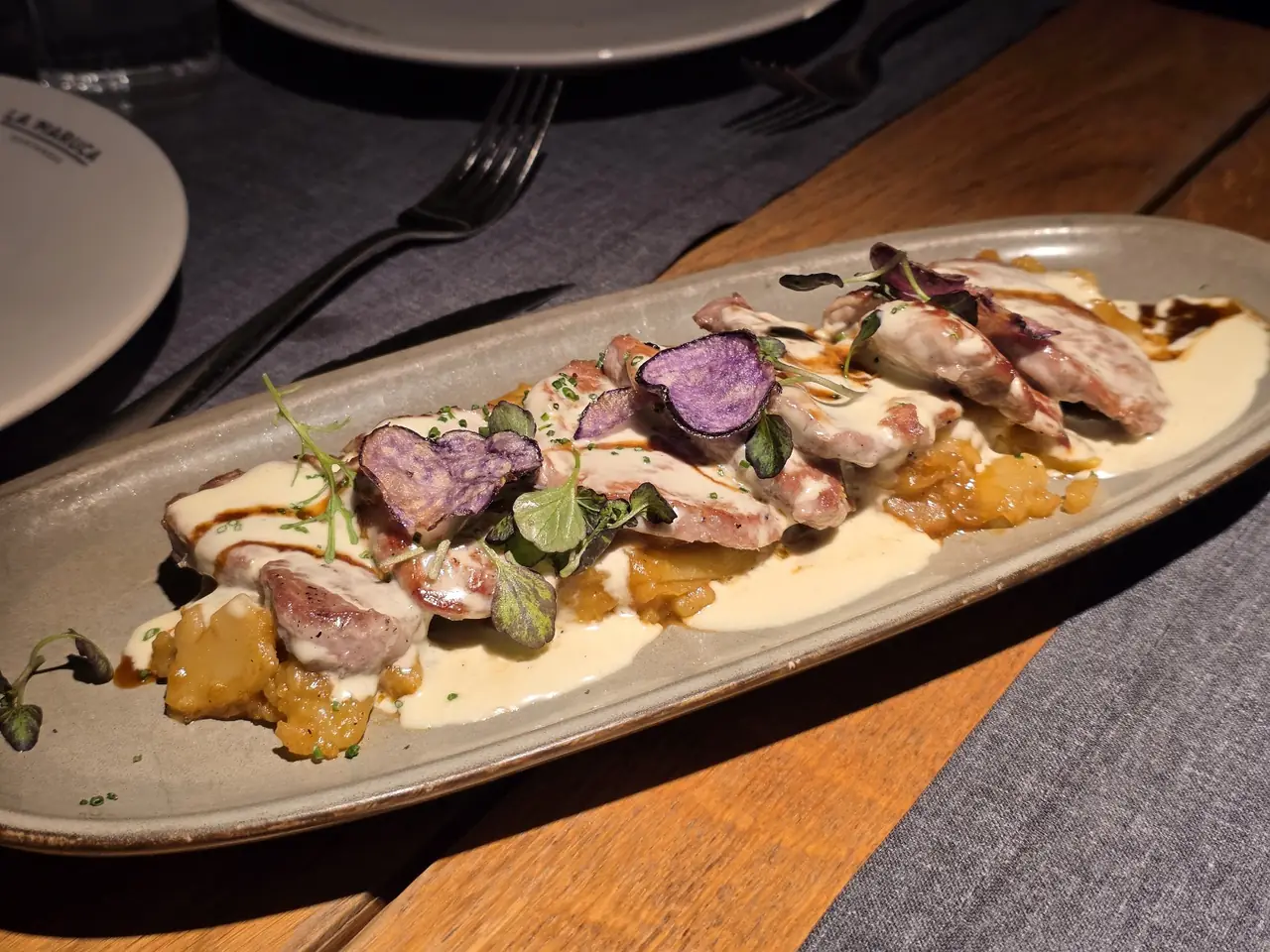 Sliced pork with purple potato crisps, apple compote and cream sauce on an oval plate