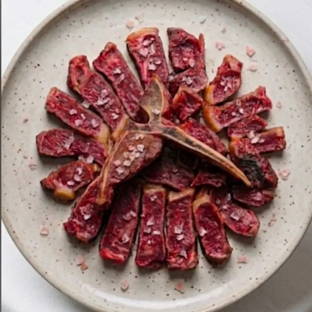 Sliced red meat arranged around a bone on a round stone-coloured plate