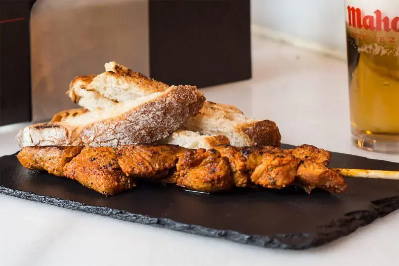 Grilled meat skewer on slate board with toasted bread and a glass of beer