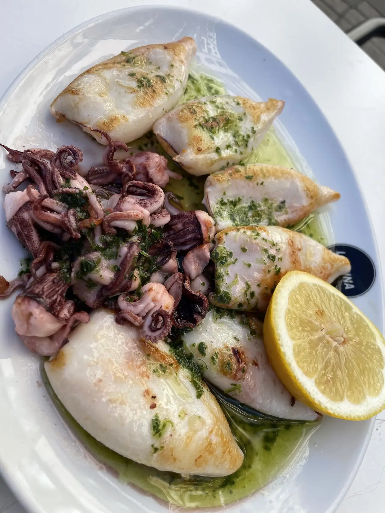Grilled squid with parsley-garlic sauce, lemon half on a La Mina plate