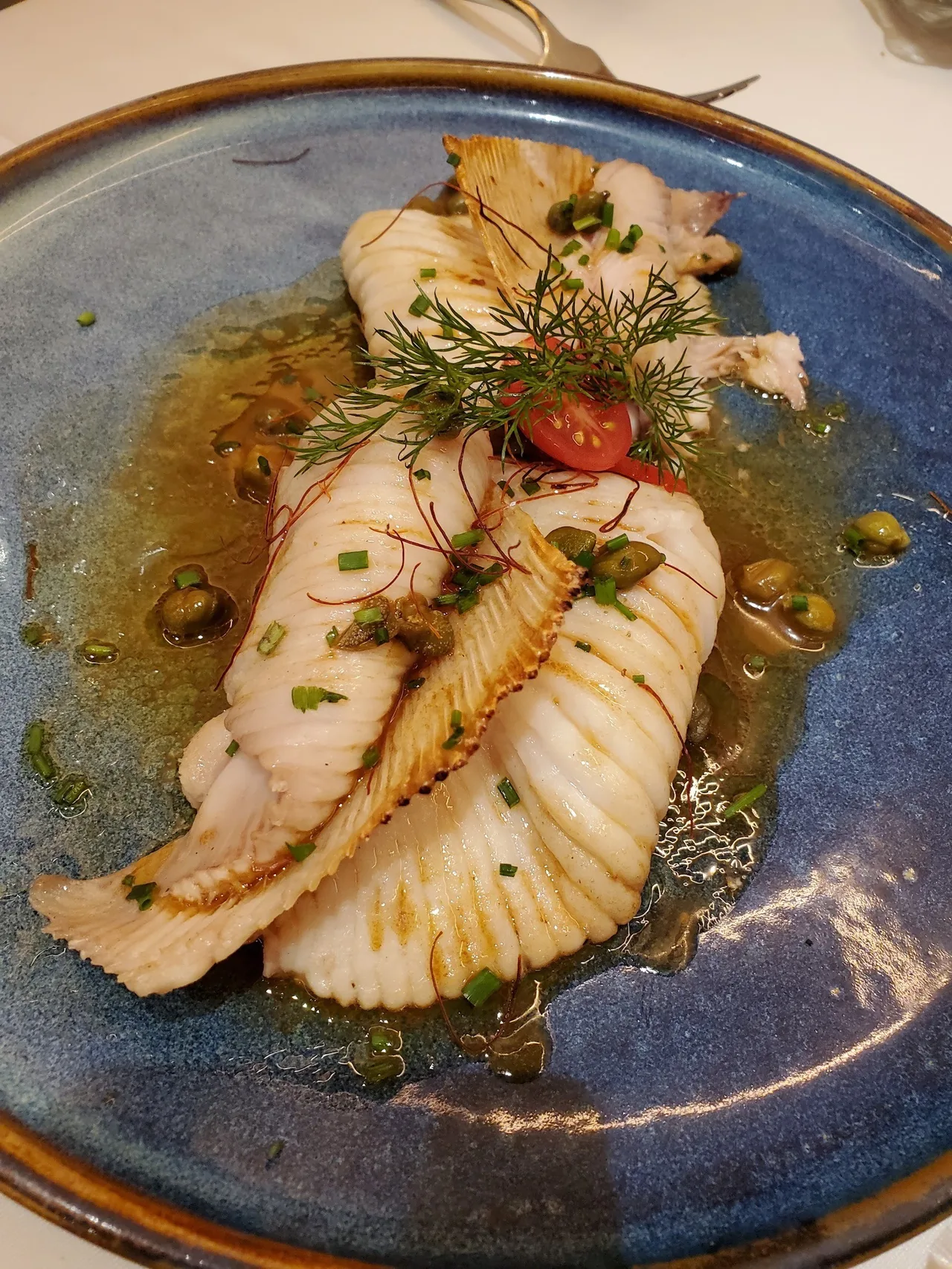 A blue-glazed plate of pale folded slices in a golden sauce with herbs