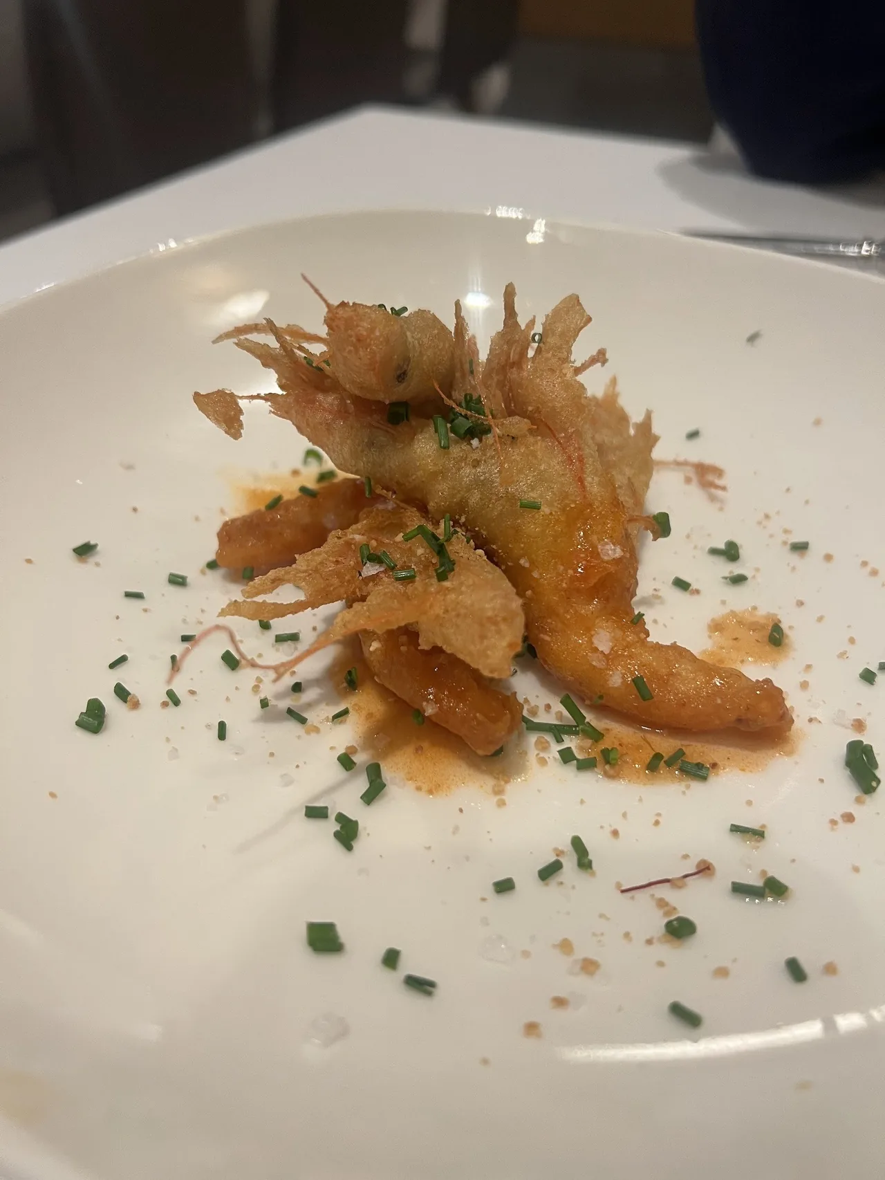 A white plate of fried golden pieces with a flaky topping and chives