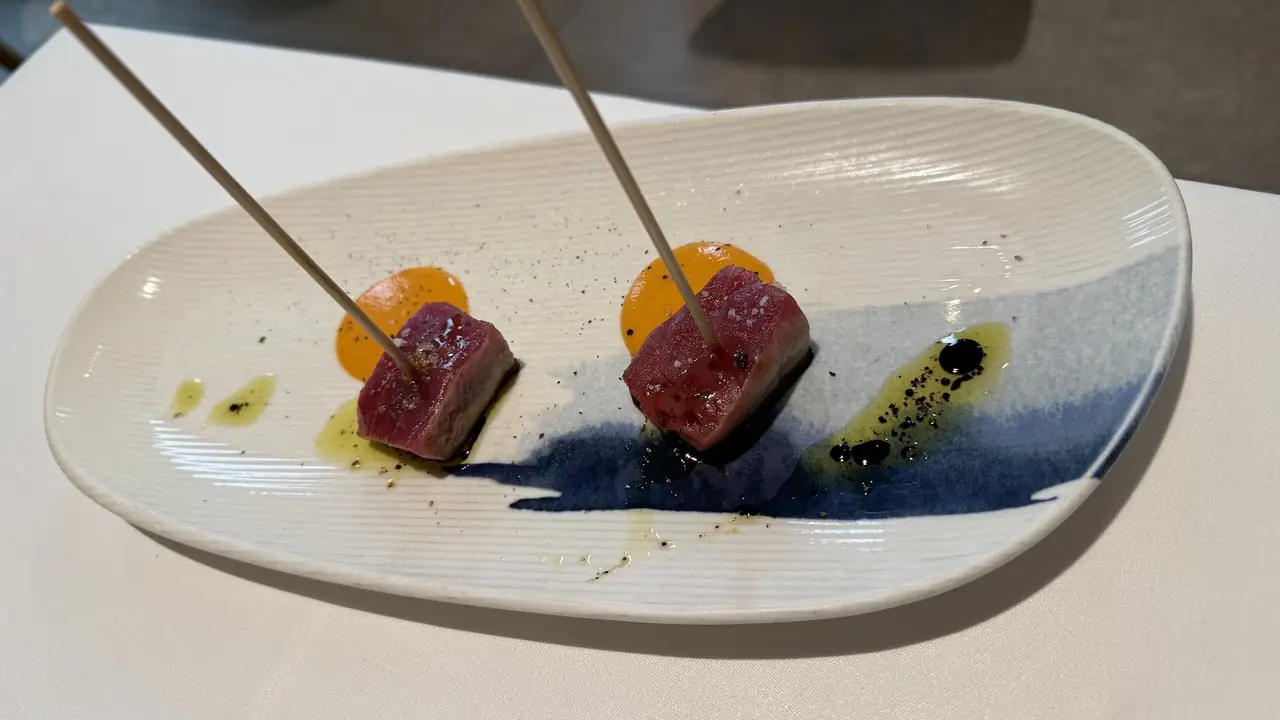 Two skewered cubes of seared meat with orange and black sauce accents on an artistic plate