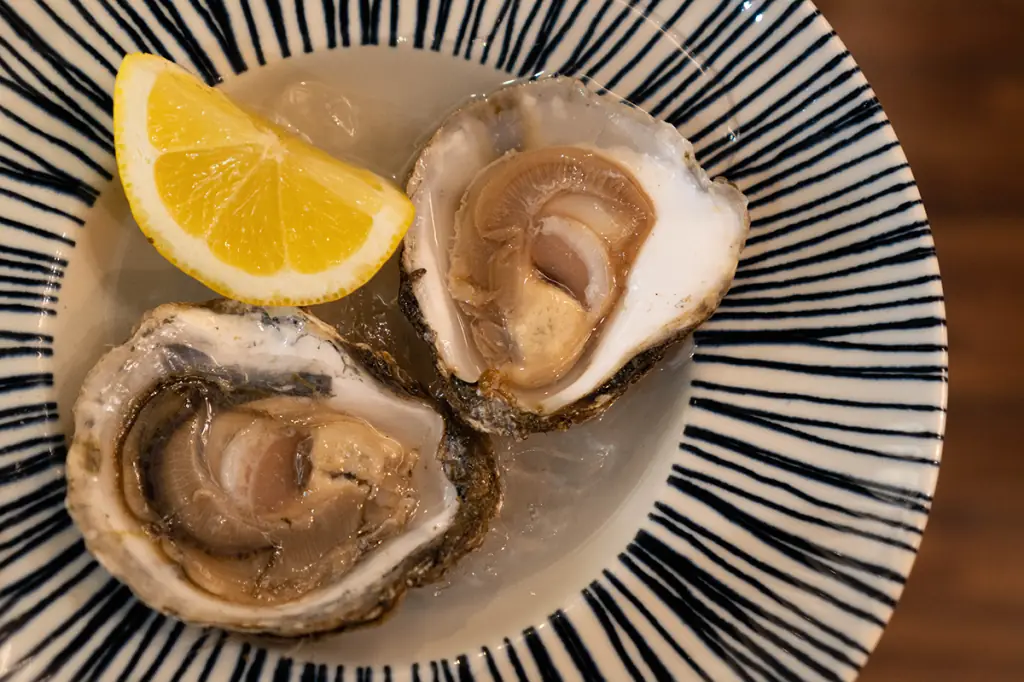 Two freshly shucked oysters on the half shell with a lemon wedge, served on a striped ceramic plate at La Moreneta