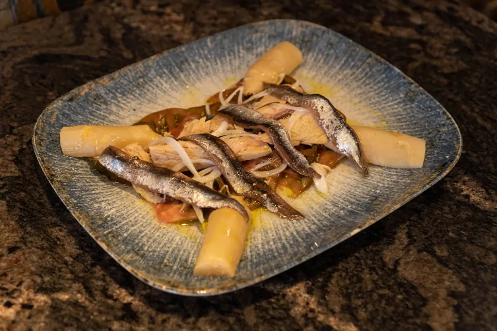 Marinated anchovies with sliced white asparagus and tomato on a striped blue-and-white plate at La Moreneta