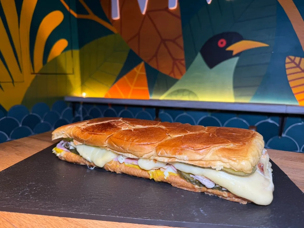 A long toasted sandwich with melted cheese on a dark board