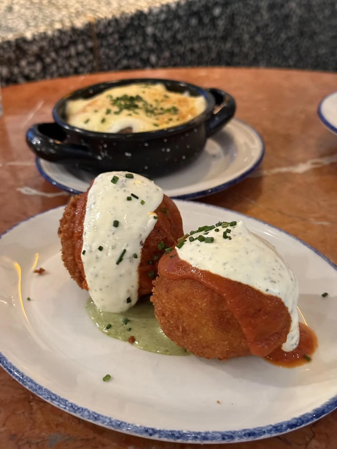 Two breaded croquettes on a plate with a creamy sauce