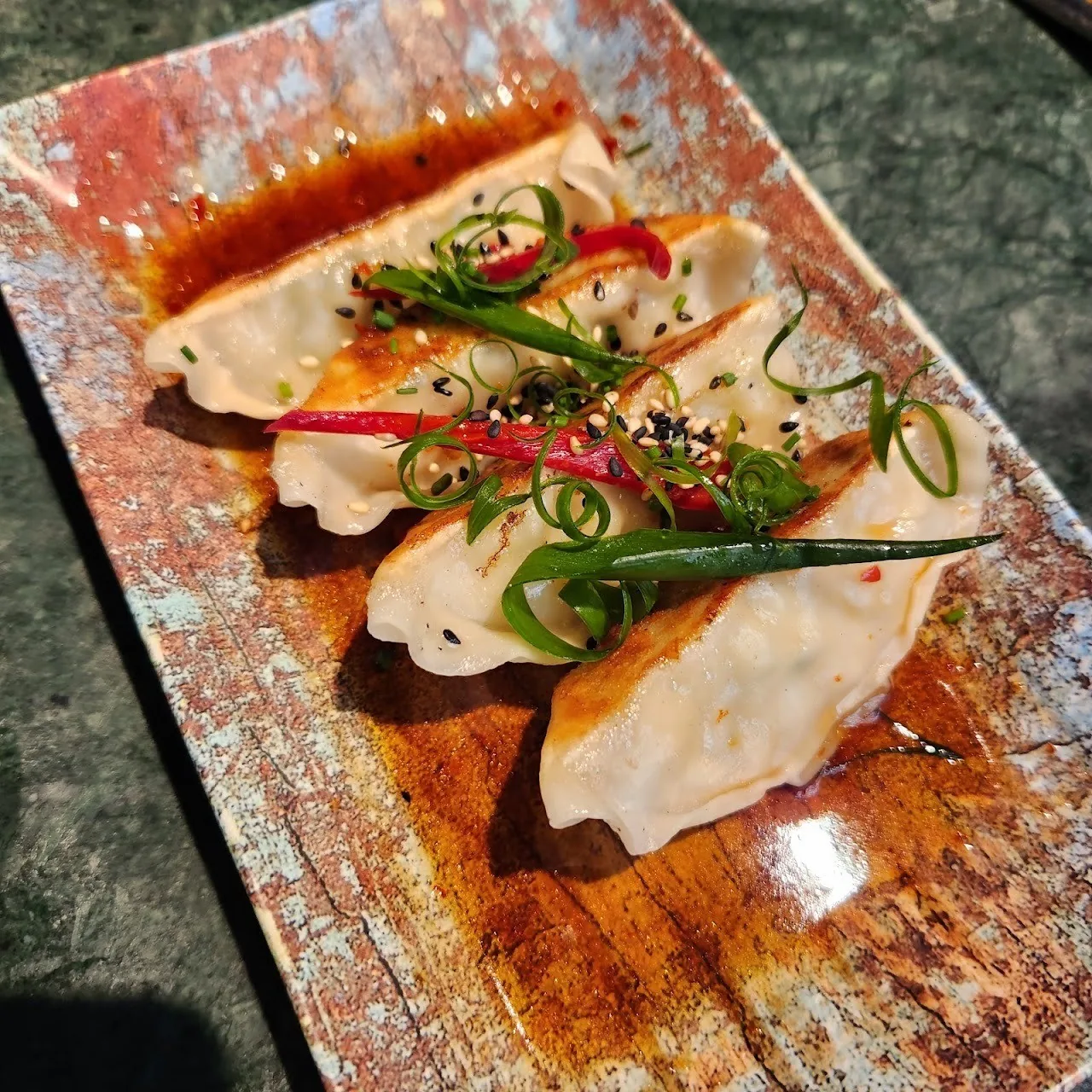 Folded dumplings topped with chopped spring onion and sauce on a patterned plate