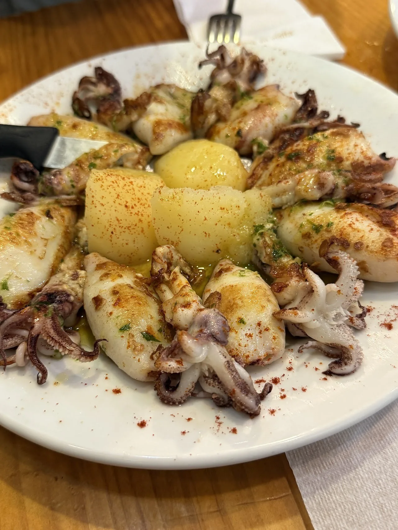 A white plate of grilled squid with a boiled potato