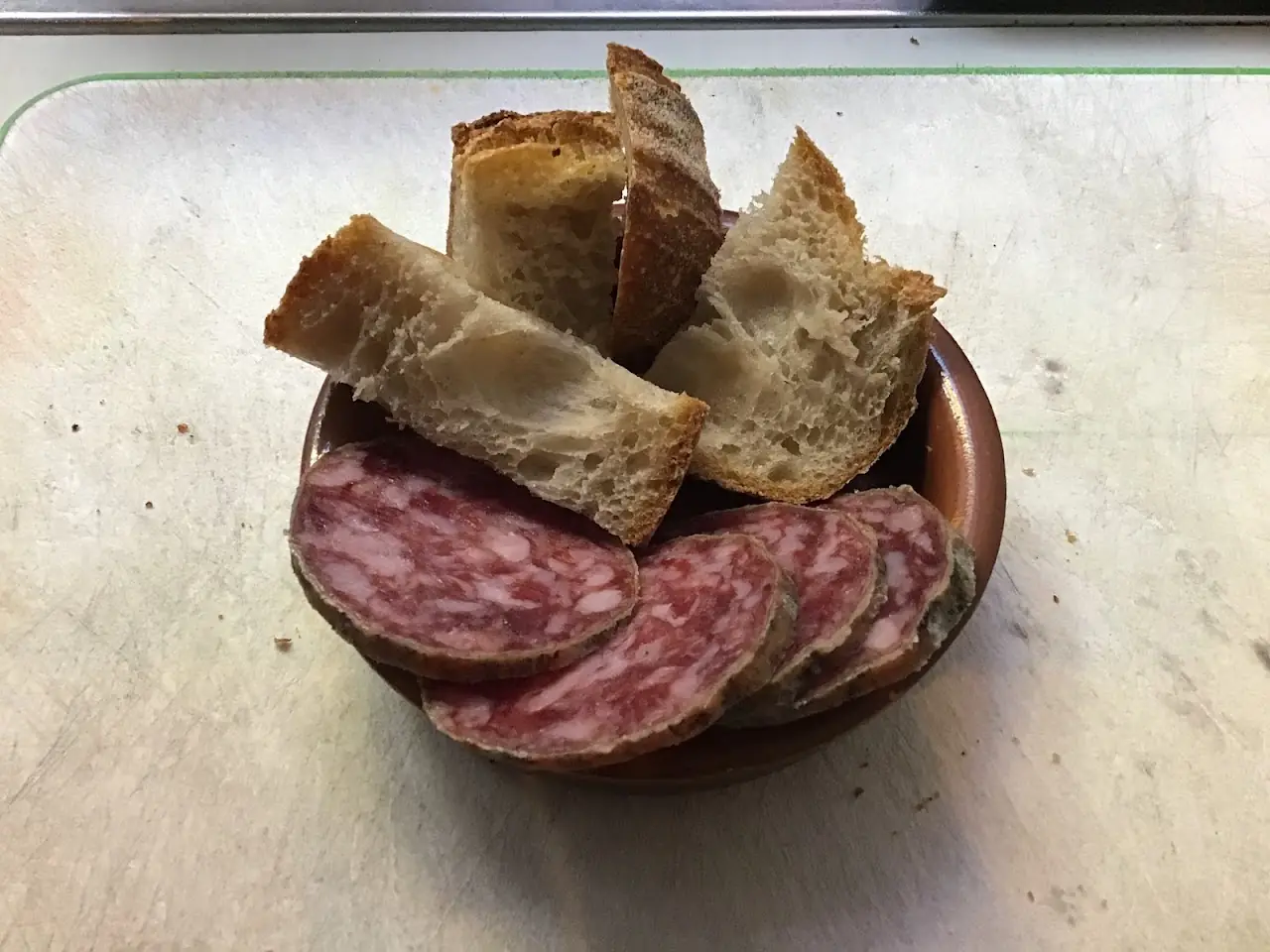 Sliced cured sausage and torn bread on a small wooden board.