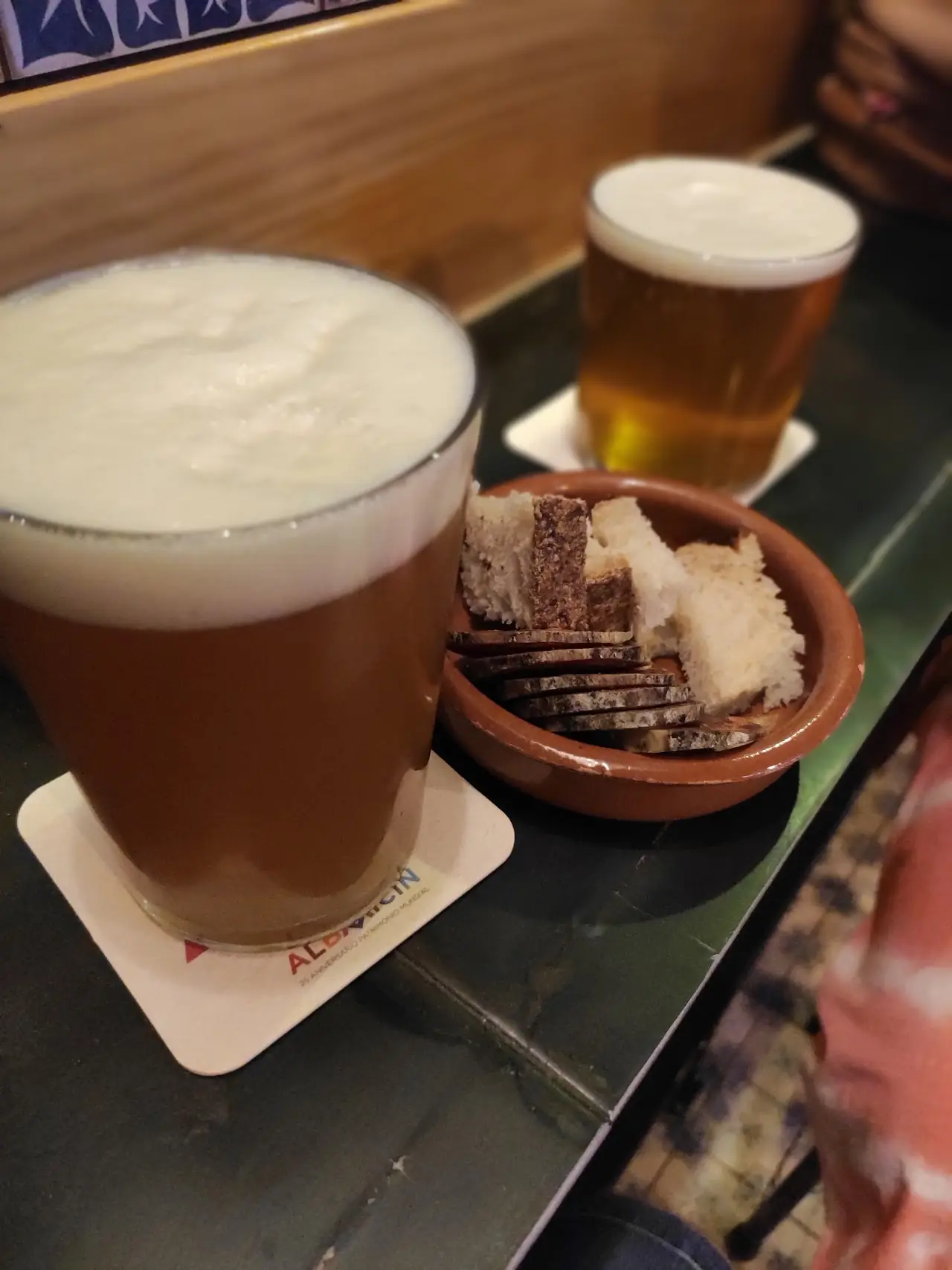 A glass of beer with foam head next to a small bowl of crackers.