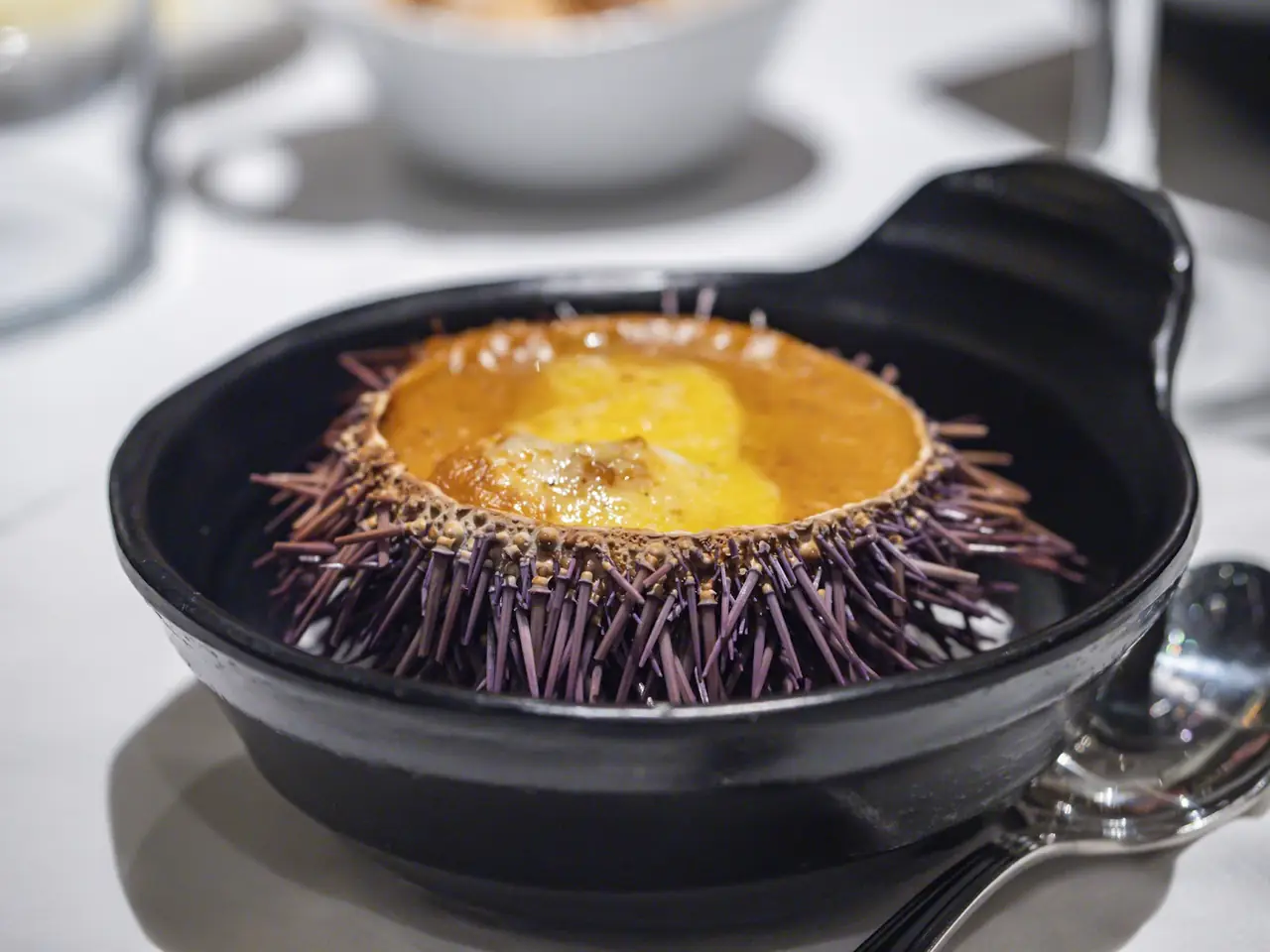 Sea urchin baked in its shell, served in a small black cazuela with a spoon