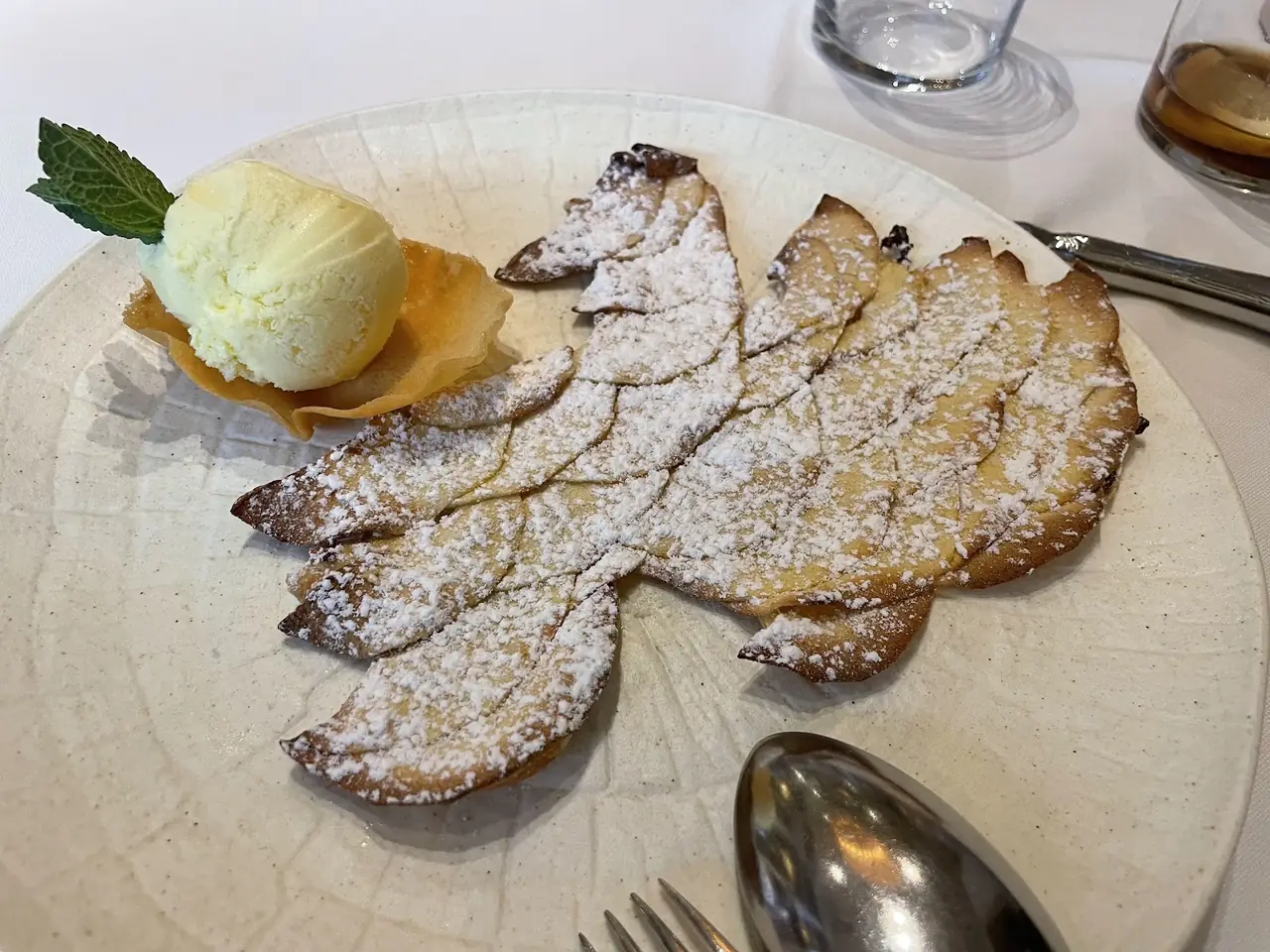 Dessert of a thin leaf-shaped baked pastry dusted with powdered sugar next to a scoop of vanilla ice cream