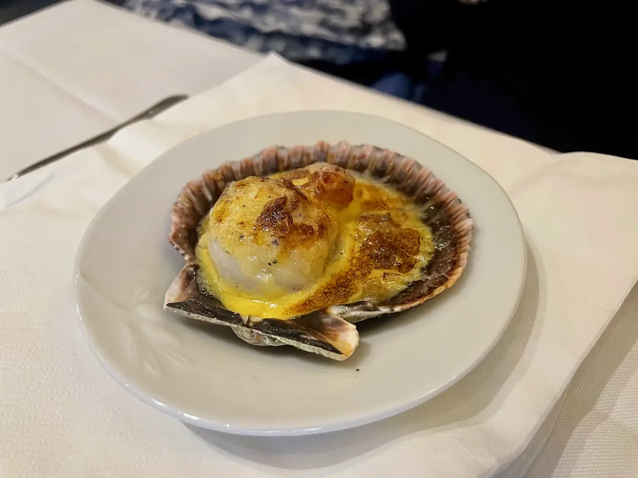 Scallop gratineed with a browned sauce, served in its shell on a white plate