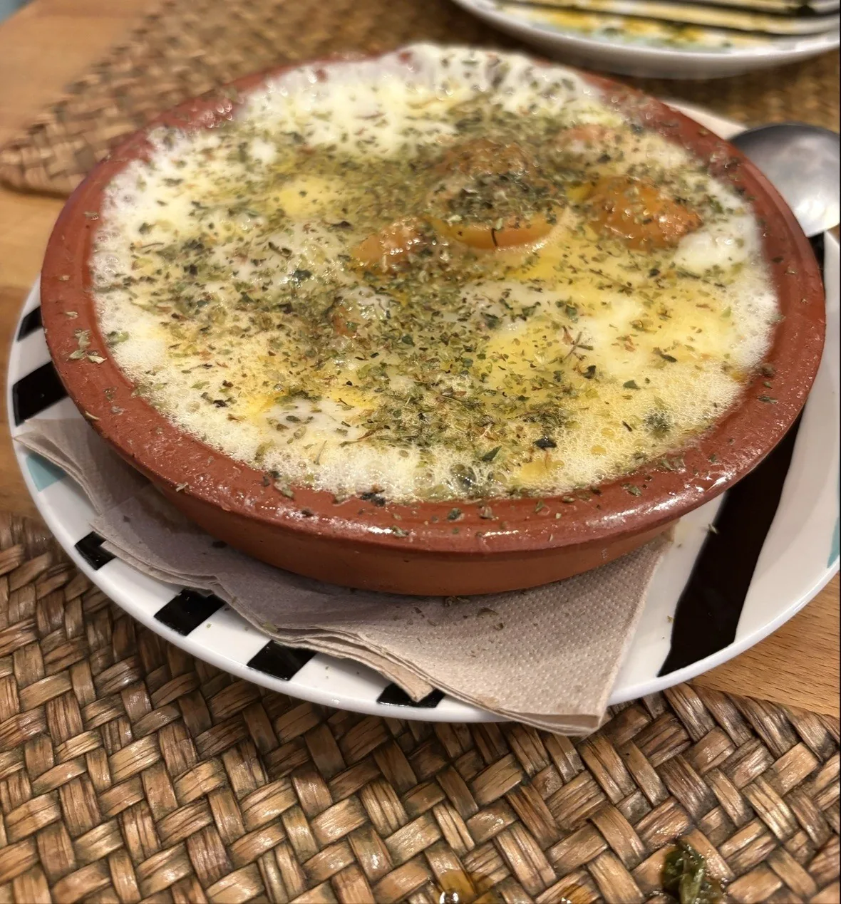 A clay dish of melted, browned cheese with herbs