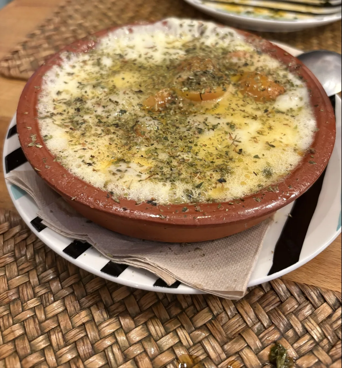 A baked cheese dish topped with herbs in a clay bowl