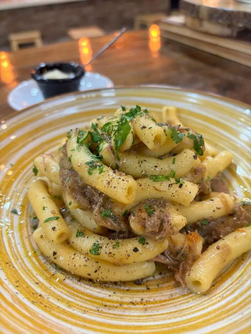 Tubular pasta with shredded braised meat, herbs and black pepper on a yellow-rimmed plate in a candlelit dining room
