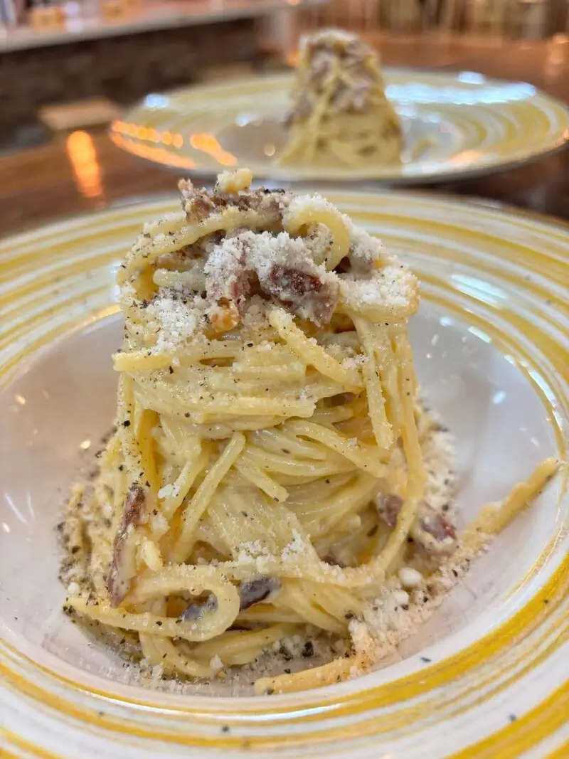 Tall twirl of spaghetti carbonara with grated cheese, black pepper and guanciale on a yellow-ringed plate