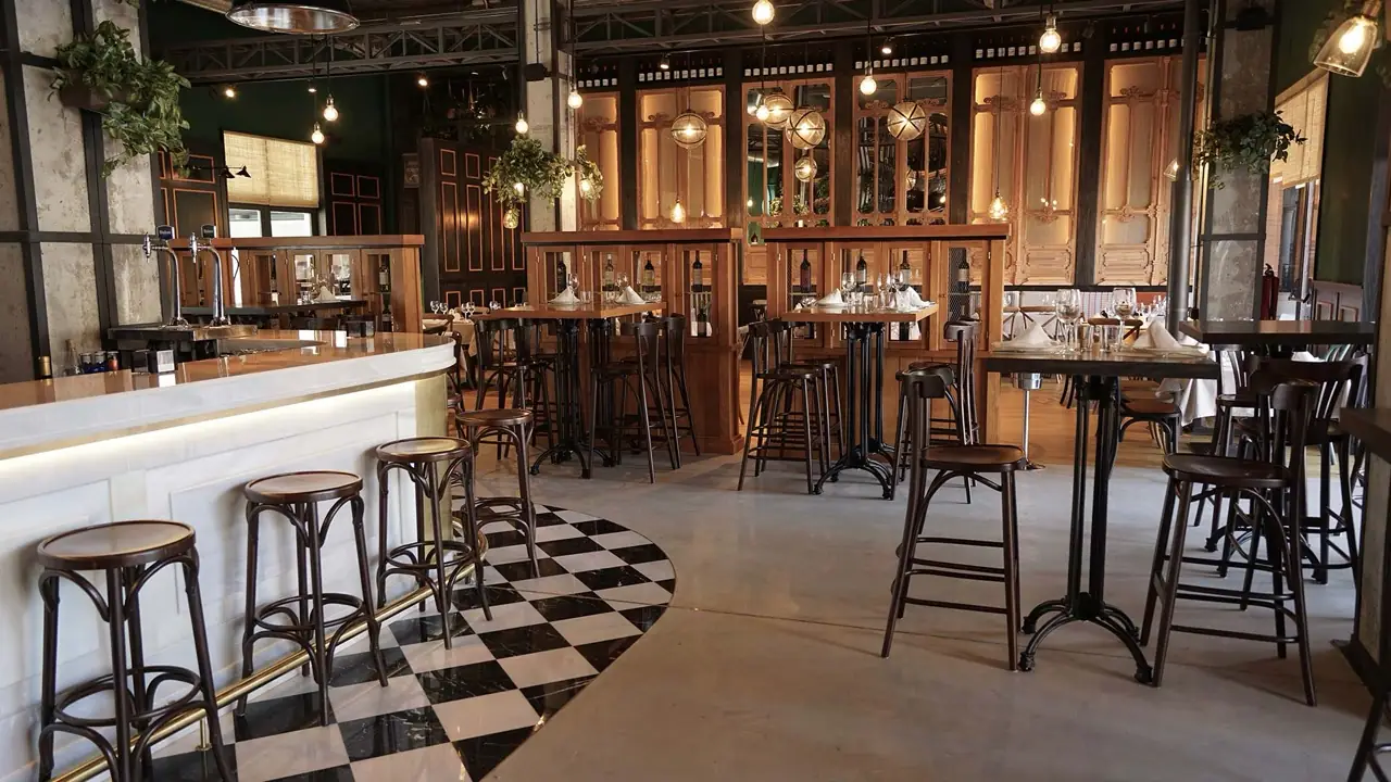 Restaurant bar and dining area with a white marble bar counter, wooden stools, black-and-white checkered floor inlay, wine cabinets, and pendant lights.