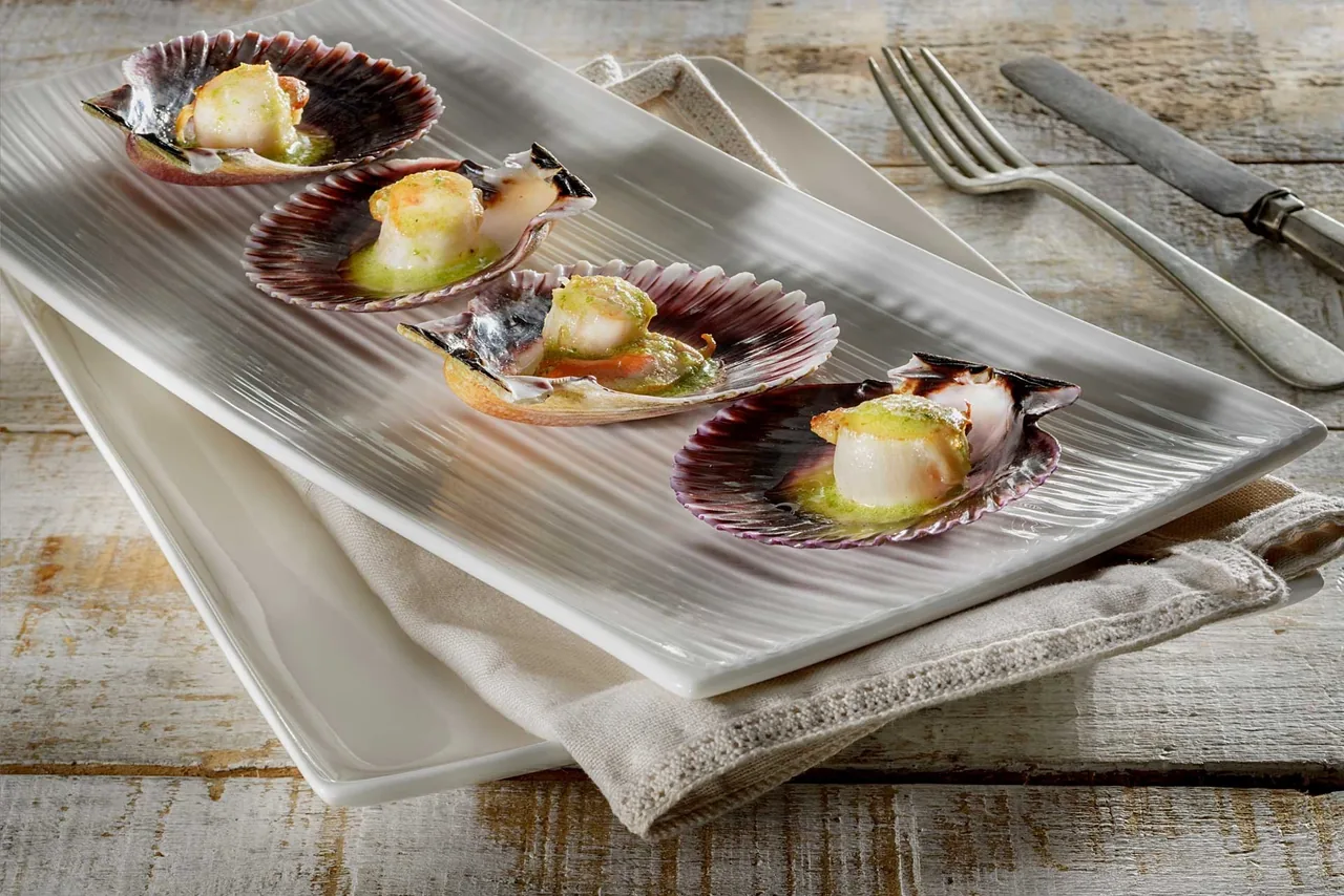 Scallops in their shells on a long white plate on a wooden table