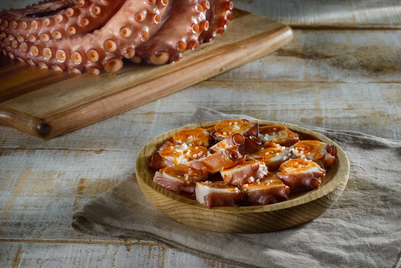 Octopus pieces in a wooden bowl beside a whole tentacle on a board