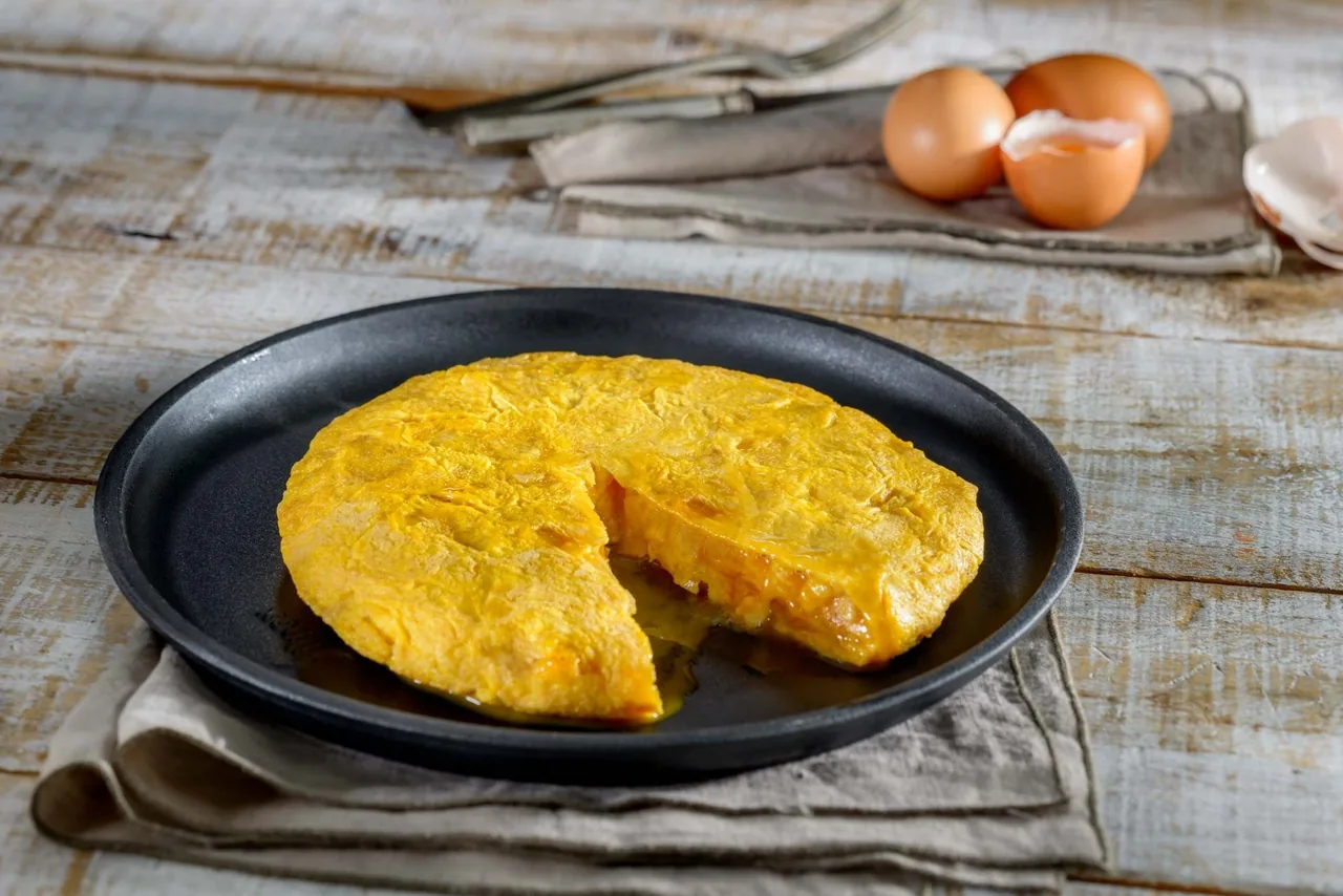 A potato omelette with a slice cut out on a black pan