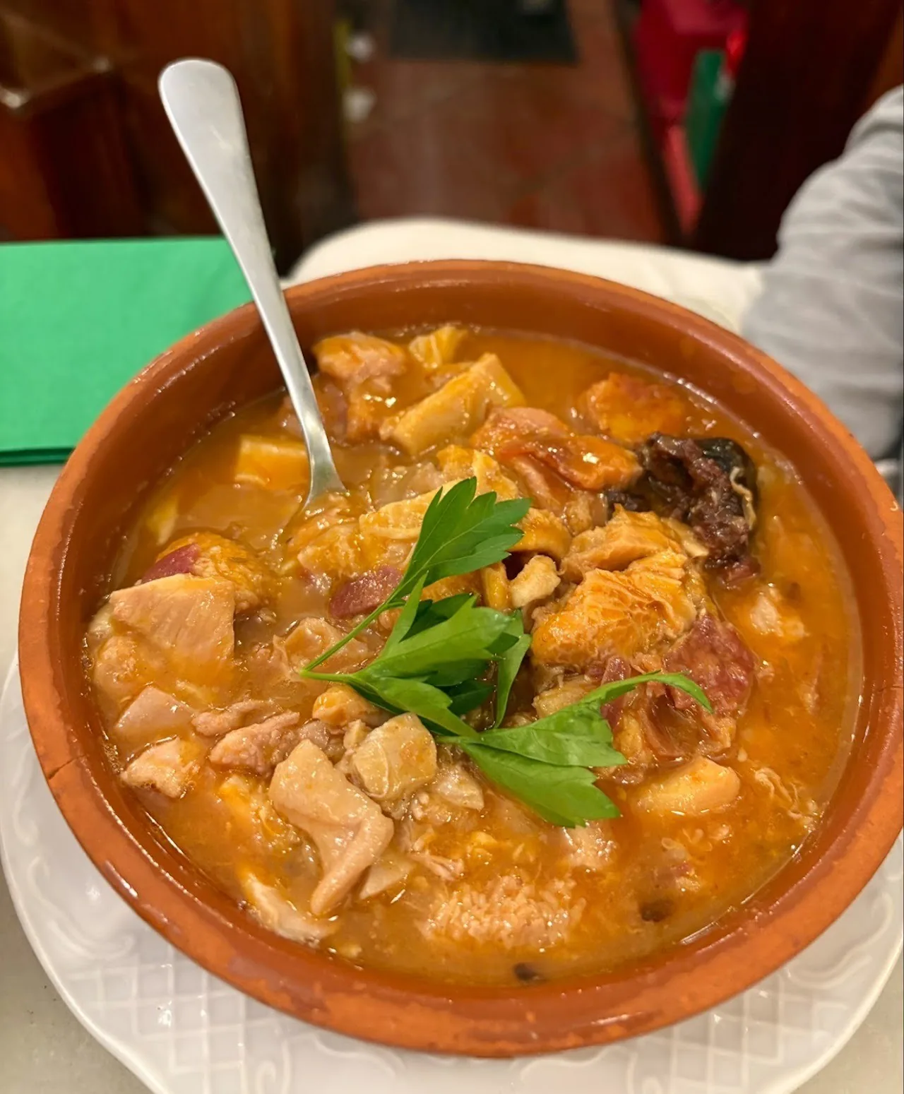 A terracotta bowl of a golden stew with chunks of meat and a sprig of parsley