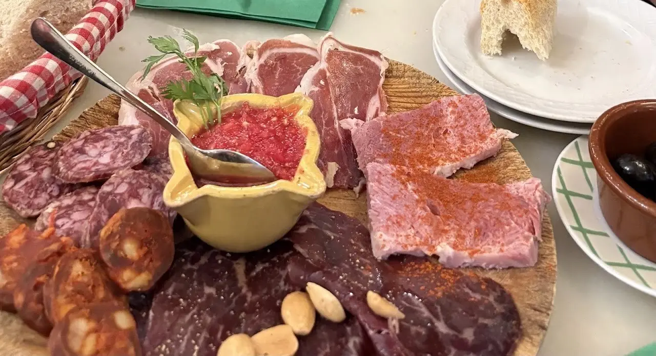A wooden board of cured meats, chorizo and cecina with a small dish of grated tomato and almonds