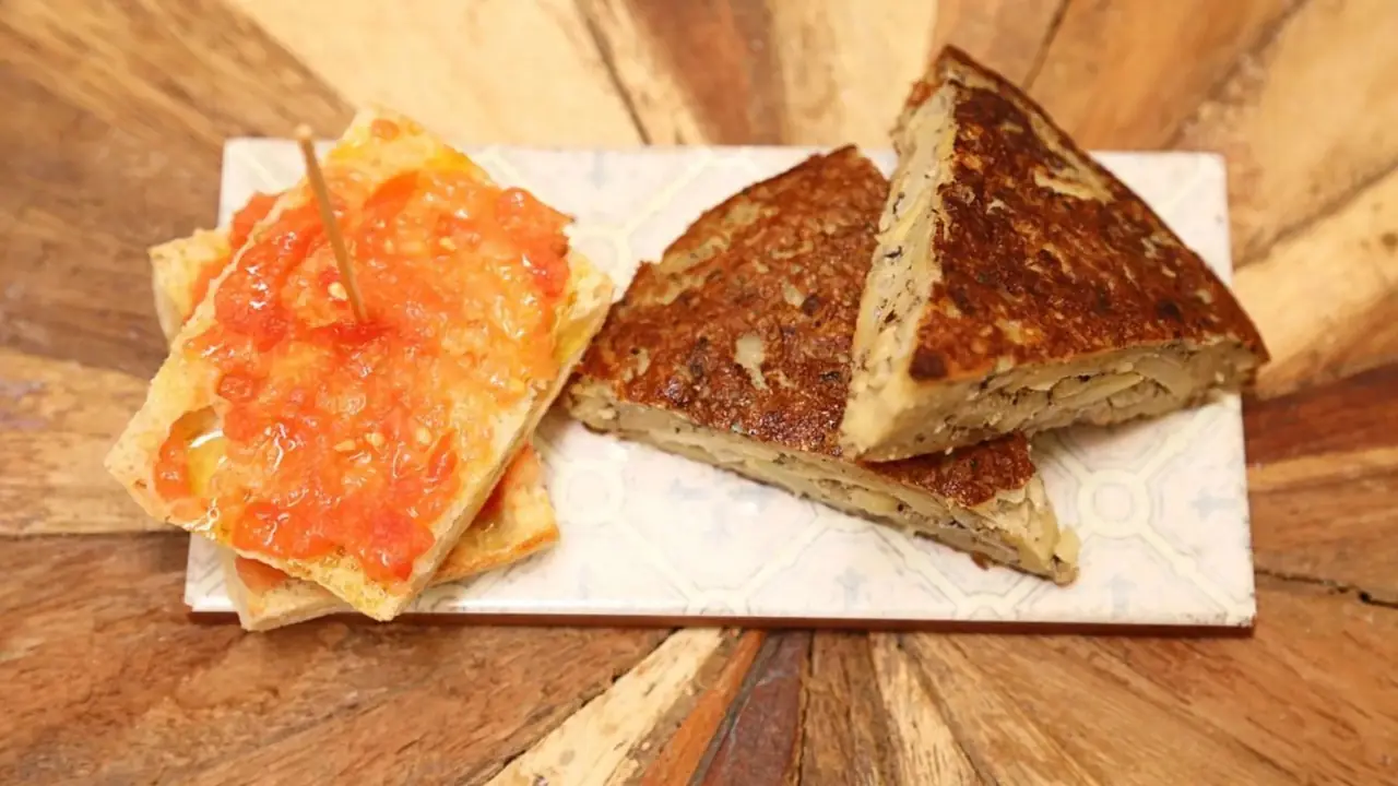 Sliced vegan Spanish tortilla wedges next to toasted bread topped with grated tomato at La Perra Verde