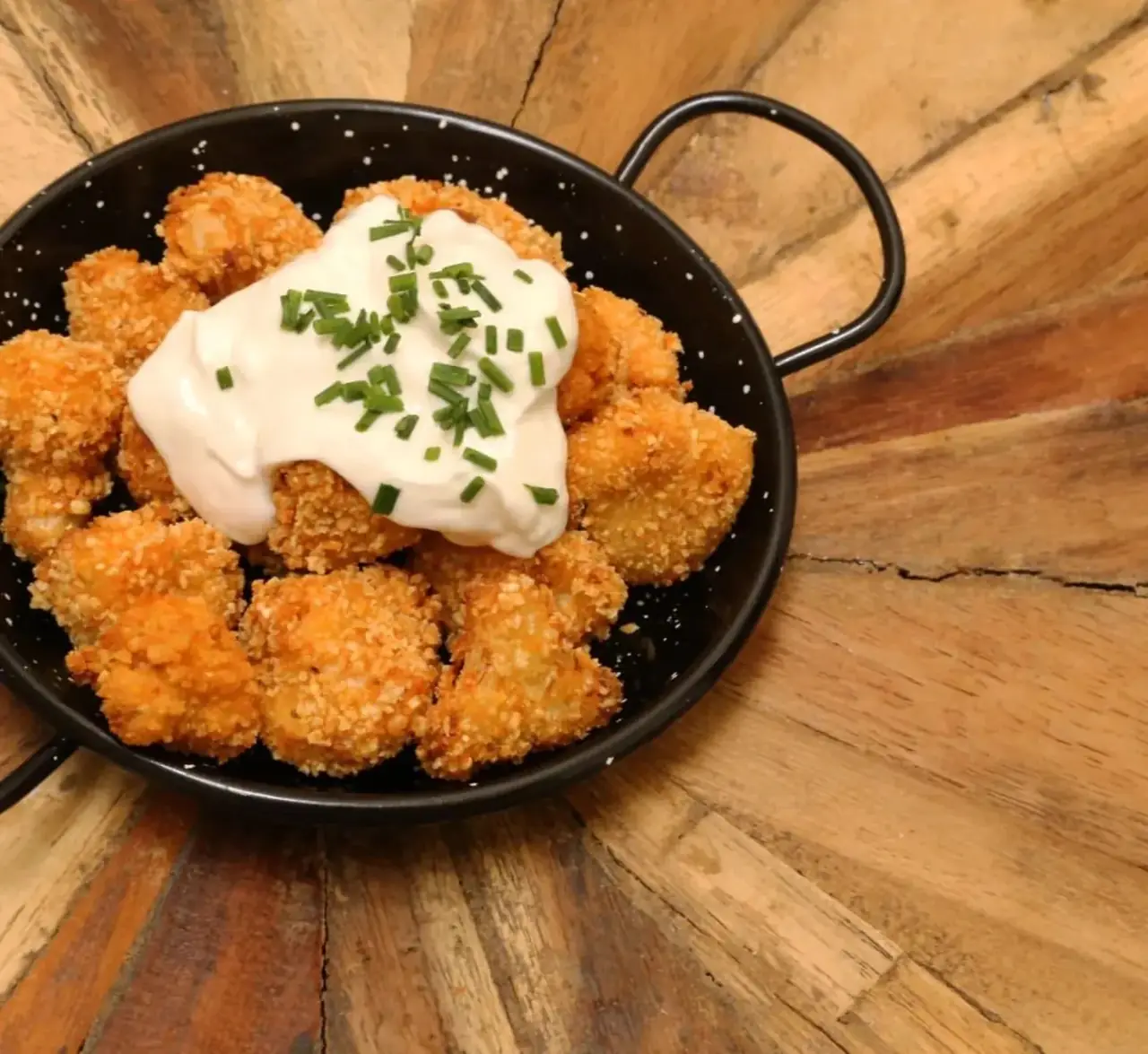 Breaded fried bites topped with a dollop of sauce and chopped chives in a black pan at La Perra Verde