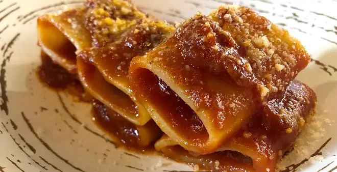 Paccheri pasta coated in rich tomato ragu with grated cheese on a rustic plate