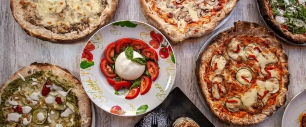 Overhead spread of several pizzas around a plate of tomato, mozzarella and basil