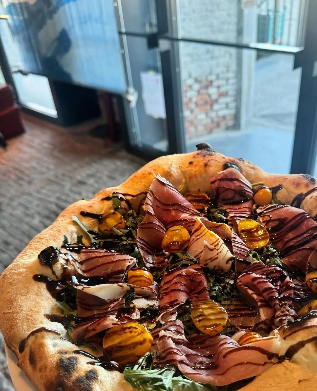 A pizza with cured meat slices and orange pieces on top, seen from above
