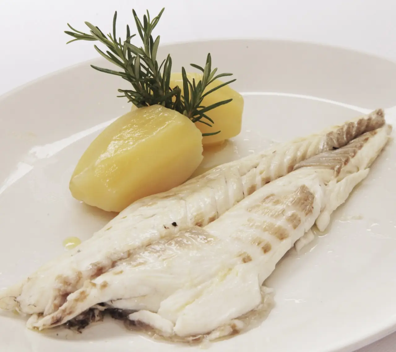 Grilled white fish fillet served with steamed potato wedges and a fresh rosemary sprig on a white plate.