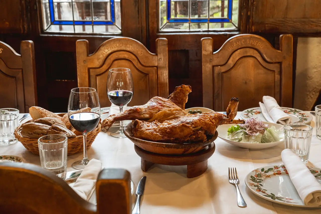 Whole roasted suckling pig served on a wooden dish with bread, salad and glasses of red wine on the table