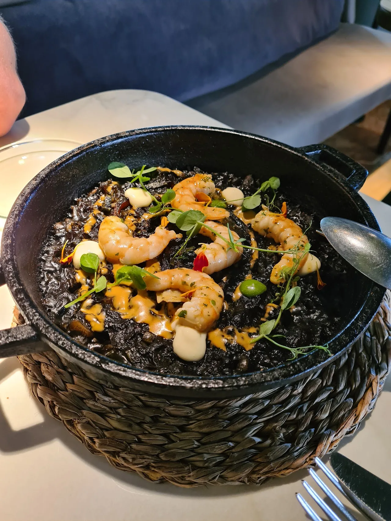 A black pot of rice with shrimp and green herbs