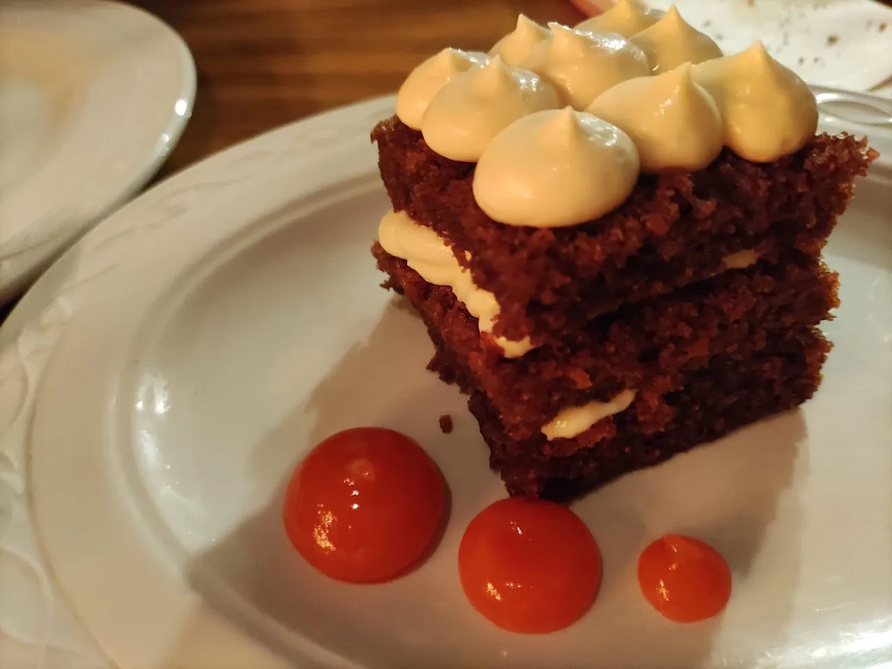 A two-layer red velvet cake with cream dollops and cherry tomato garnish