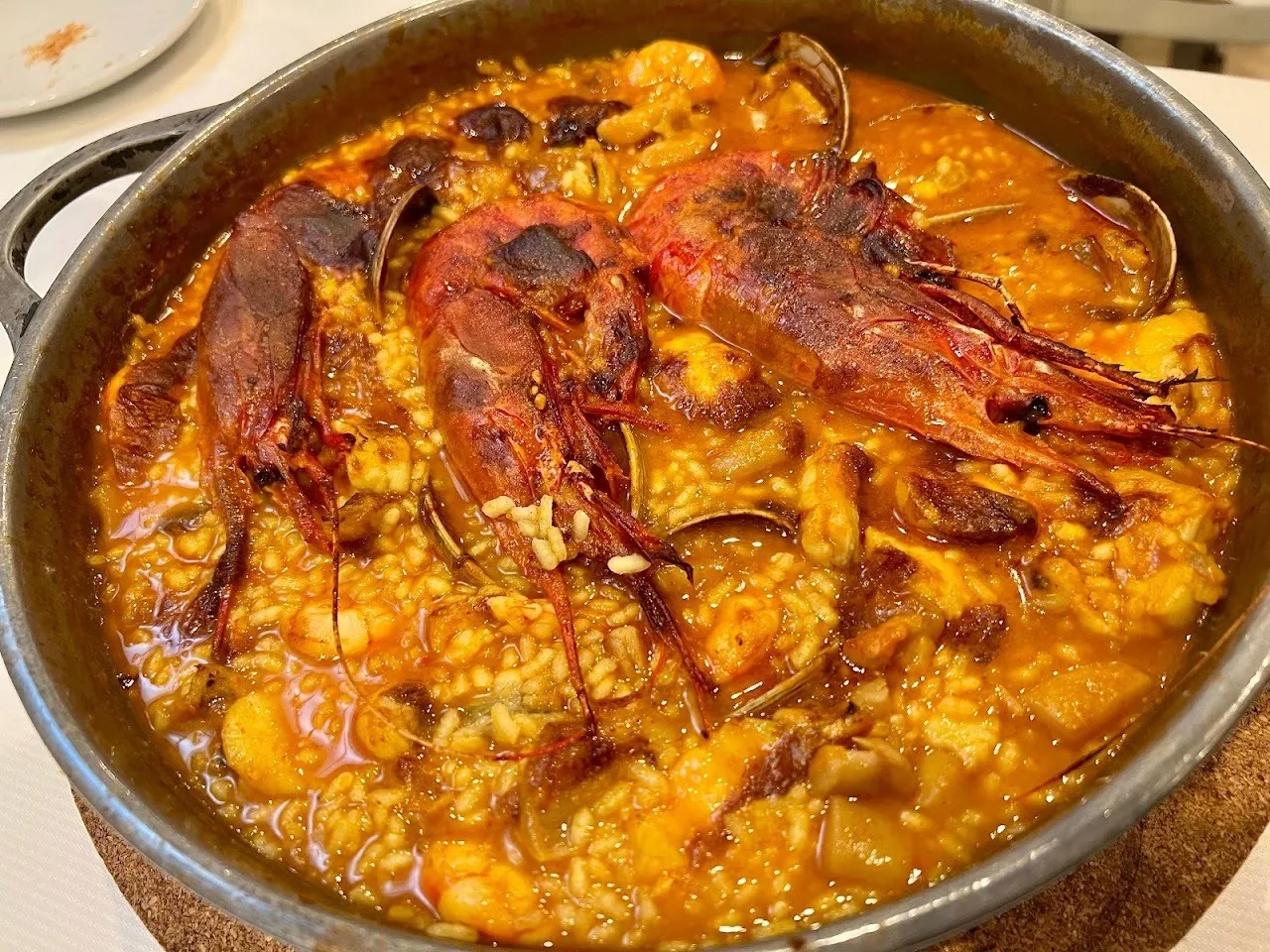 A wide pan of orange rice topped with large red prawns