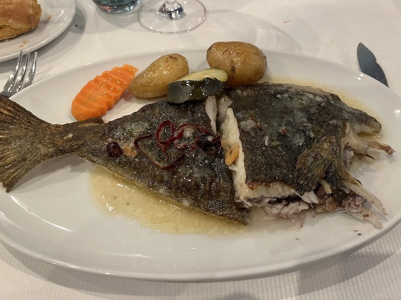 A whole flat fish with potatoes and carrot slices on a white plate